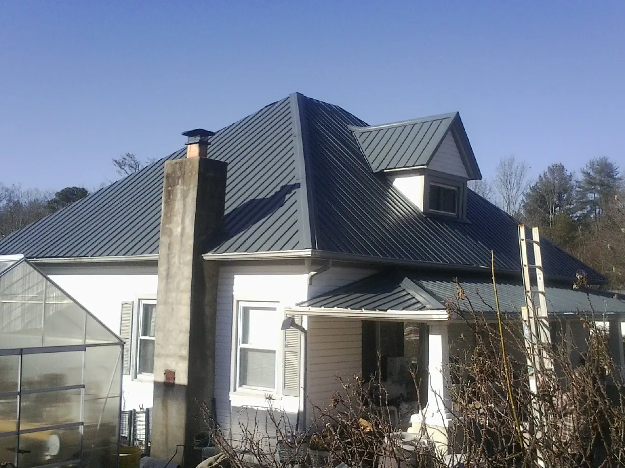 Dark blue standing seam metal roof on a white farmhouse with dormer — Slate & Tile Roof Repair by Roofing Brothers in Fruitland Park