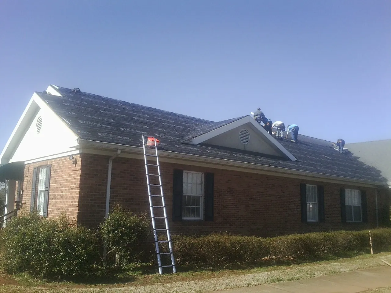 Crew tearing shingles off a brick ranch roof with a ladder set — Emergency Roof Repair work by our crew in Fruitland Park