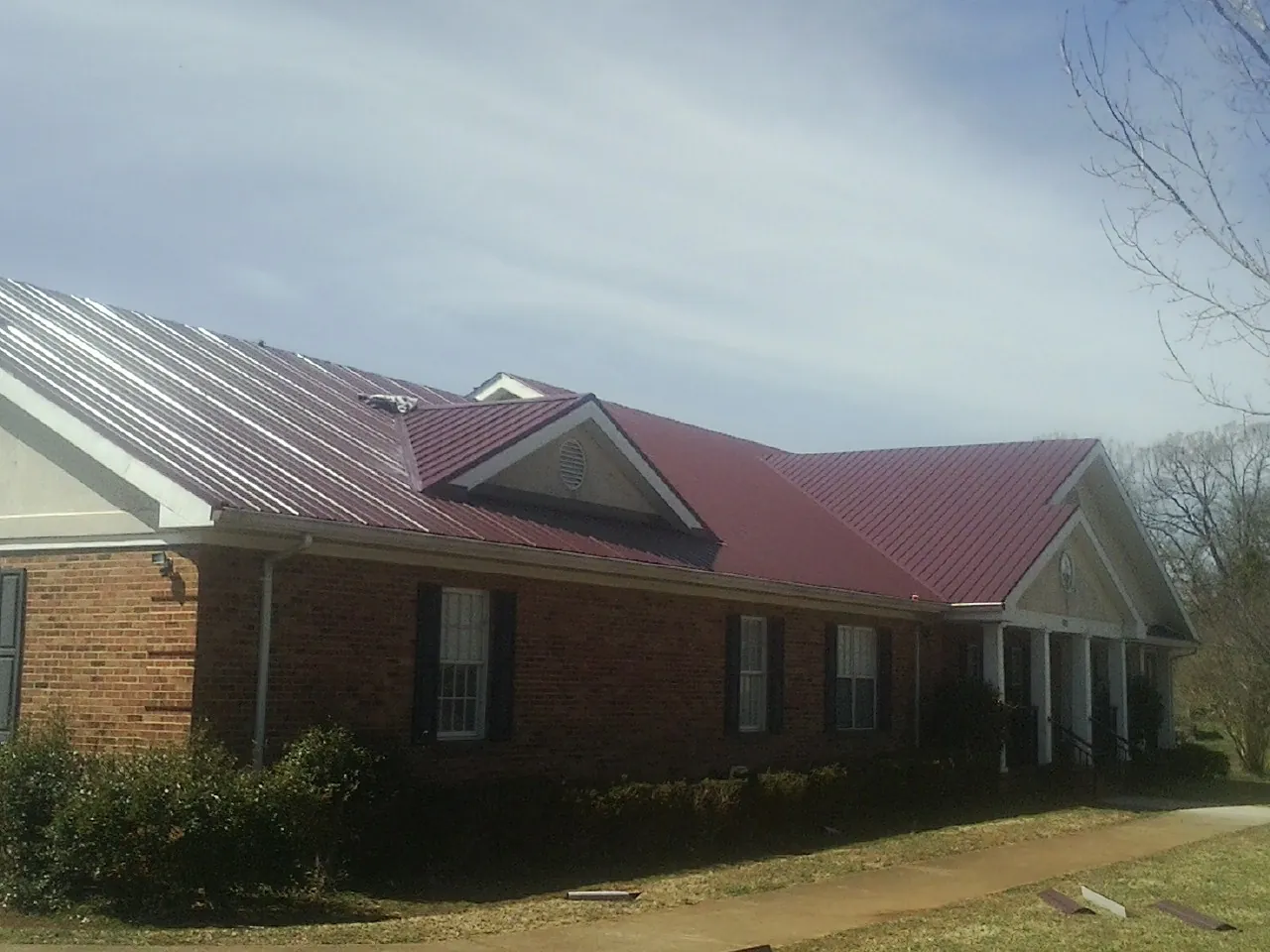 Red metal roof with gabled entries on a long brick building, from a Hail Damage Roof Repair job in Fruitland Park