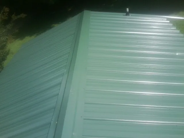 New green metal panels meeting at the ridge of a roof — Flat Roof Repair work by our crew in Fruitland Park