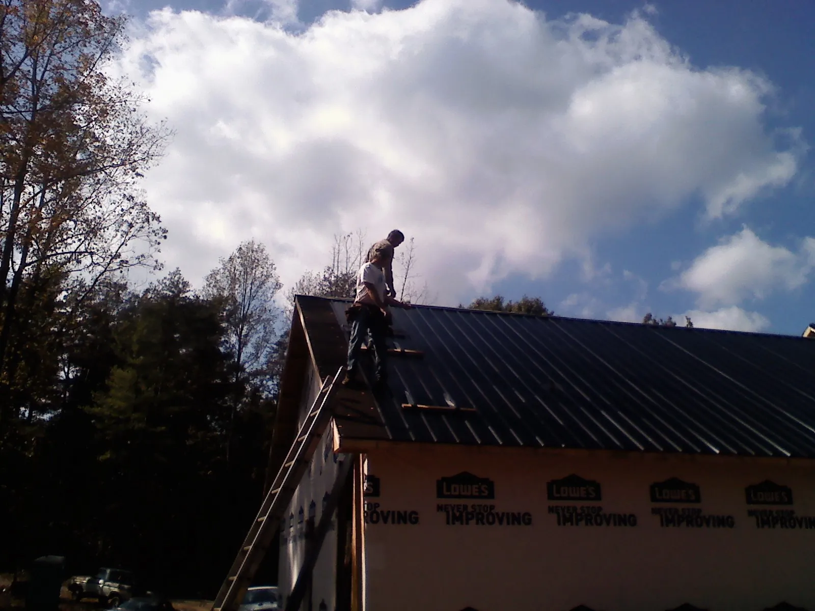 Roofer fastening dark metal panels high against a cloudy sky, from a Roof Inspection job in Fruitland Park