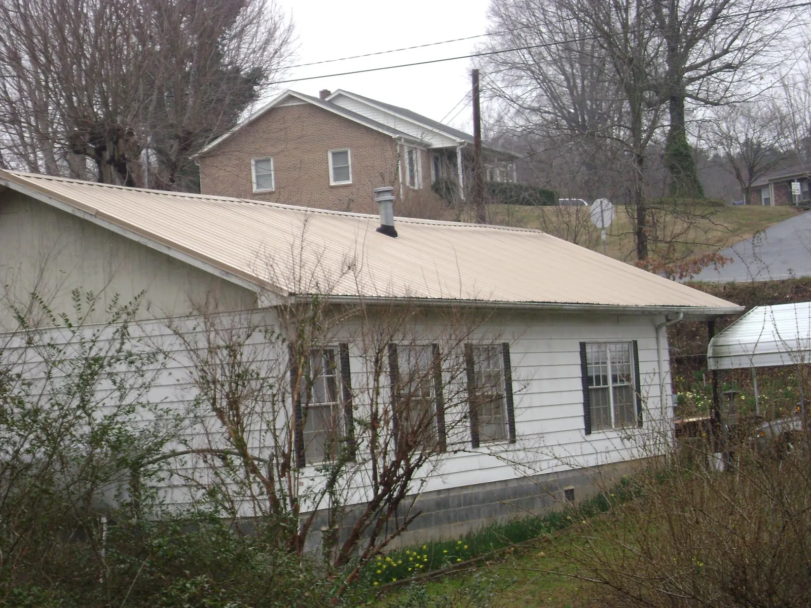 Tan metal roof on a white sided house set into a hillside — Commercial Roofing by Roofing Brothers in Fruitland Park